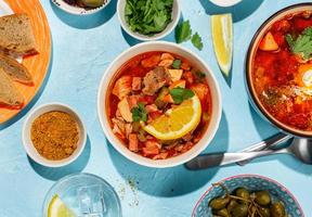 Home cooked solyanka meat soup served with lemon, olives and capers on vibrant blue background photo