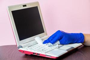 desinfección y limpieza de la computadora portátil y las superficies del hogar sobre fondo rosa foto