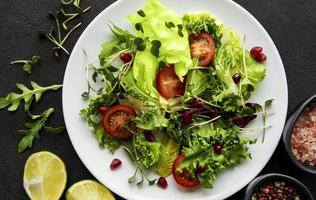 Fresh green mixed salad bowl with tomatoes and microgreens on black concrete background photo