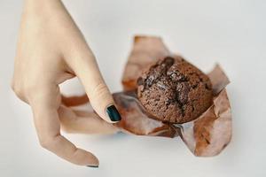 Woman's hand picks up chocolate cupcake from table photo