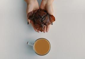 muffin de chocolate en manos de mujer y una taza de café caliente junto a él foto
