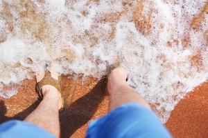 Man in flip-flops stands in sand in an ocean wave photo