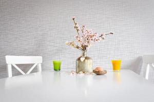 Bouquet style white kitchen table set up with yellow and green cups, blooming daisy flowers and an Easter egg photo