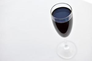 Small glass of red wine on a white background with shadows photo