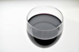 Gran vaso de vino tinto sobre un fondo blanco. foto