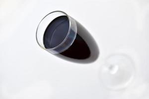 Vaso pequeño de vino tinto sobre un fondo blanco con sombras foto