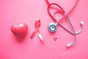 Red ribbon, heart toy, and stethoscope on pink background photo