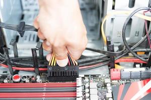 La mano del hombre sosteniendo un enchufe y un cable para conectarlo a una computadora de placa base foto