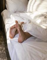 Feet of a sleeping person sticking out from under a warm and comfortable blanket on the bed, bare heels photo