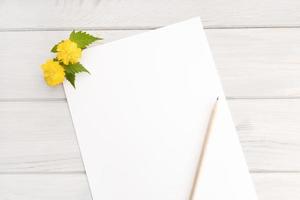 Blank white paper, yellow flower branch on wooden table. Springtime background. Mock up copy space top view photo
