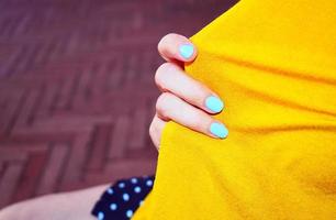 A person with blue manicure nails holding an orange textile photo