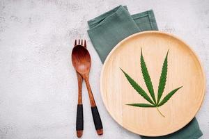 Food conceptual image of a hemp leaf with a spoon and fork on white concrete background photo
