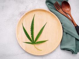 Food conceptual image of a hemp leaf with a spoon and fork on white concrete background photo
