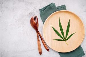 Food conceptual image of a hemp leaf with a spoon and fork on white concrete background photo