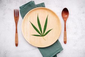 Food conceptual image of a hemp leaf with a spoon and fork on white concrete background photo