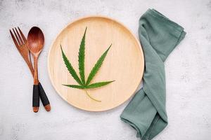 Food conceptual image of a hemp leaf with a spoon and fork on white concrete background photo