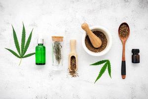 Glass bottle of hemp oil with a white mortar and hemp leaves set up on a concrete background, aromatherapy concept photo