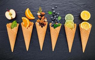 Various ingredients for ice cream flavors in cones showing blueberries, lime, pistachio, almonds, orange, chocolate, vanilla, and coffee set up on a dark stone background. Summer and sweet menu concept. photo