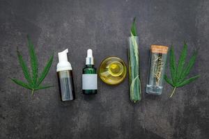 Glass bottles of hemp oil and hemp leaves set up on a concrete background photo