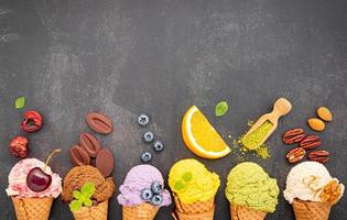 Various ice cream flavors in cones of blueberry, green tea, pistachio, almond, orange, and cherry on a dark stone background. Summer and sweet menu concept