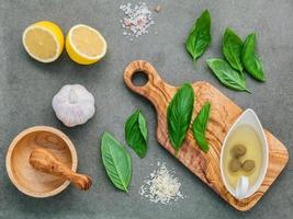 Ingredients for homemade pesto sauce of basil, parmesan cheese, garlic, olive oil, lemon, and Himalayan salt over a dark concrete background photo