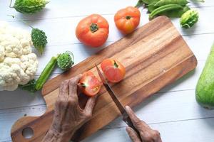 Elderly women cutting tomatoes on a chopping board top down photo