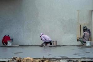 Retrato posterior de un grupo de trabajadores que utilizan paletas para pavimentar la superficie del cemento foto