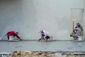 Back portrait of a group of workers using trowels for flooring the cement surface photo