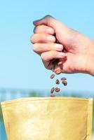 Closeup of hand releasing coffee beans into the paper brown bag photo