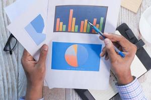 Top view of hand with pen analyzing bar chart on paper photo