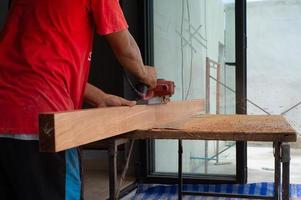 Closeup hand of carpenter holds electrical tool scrubbing the surface of wood photo