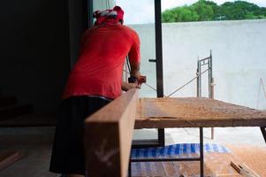 Back portrait of carpenter holds electrical tool scrubbing the surface of wood for woodwork at the construction site photo