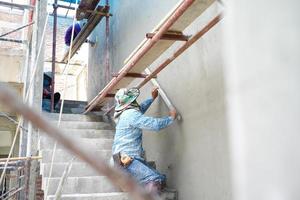 Grupo de trabajadores de pie sobre los andamios de acero y construye un muro de cemento enlucido en la casa en construcción