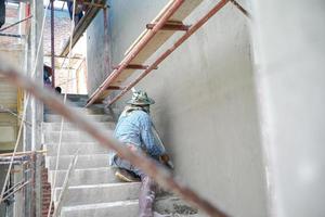 Grupo de trabajadores de pie sobre los andamios de acero y construye un muro de cemento enlucido en la casa en construcción foto