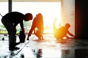 silueta grupo de trabajadores construir el piso de cemento en la casa en construcción