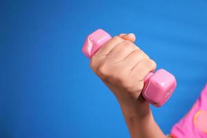 Close up of woman holding pink dumbbell on blue background