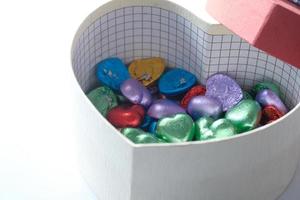 Pequeña caja de regalo en forma de corazón con caramelos sobre fondo blanco. foto
