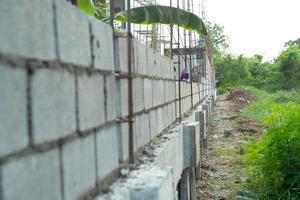 El paisaje del sitio de construcción con muro de albañil de hormigón y la mano del trabajador instalando los ladrillos en la pared en segundo plano. foto