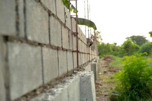 Paisaje del sitio de construcción con muro de albañil de hormigón y mano borrosa del trabajador instalando los ladrillos en la pared en segundo plano. foto