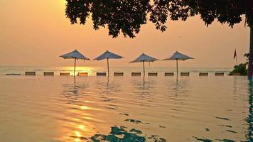 chaises de plage au bord d'une piscine au coucher du soleil