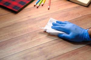 Mano en guantes de goma azul desinfectando la superficie de la mesa