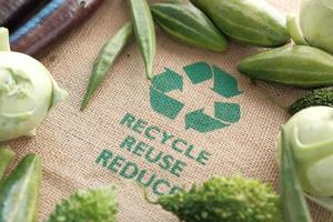 Bolsa de compras reutilizable con letrero de flechas recicladas y verduras en la mesa foto