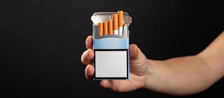 Pack of cigarettes in hand on dark background with copy space photo