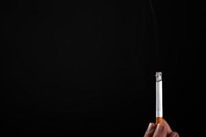 Lit cigarette in hand on a black background with copy space photo