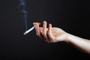 Beauty hand of a girl with a cigarette and white smoke on a dark black background photo