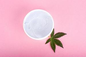Cosméticos de cannabis, crema de marihuana natural y hoja verde sobre fondo rosa. foto