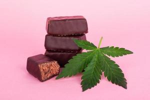 Chocolate candy with medical cannabis on pink background