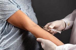 Doctor gives an injection to a sick patient in hand on a dark background photo