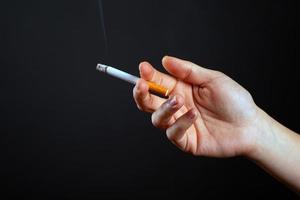 Female hand holding a smoking cigarette on a dark background photo