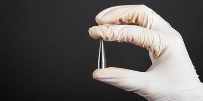 Hand in a white disposable glove holding a piercing ear expander photo
